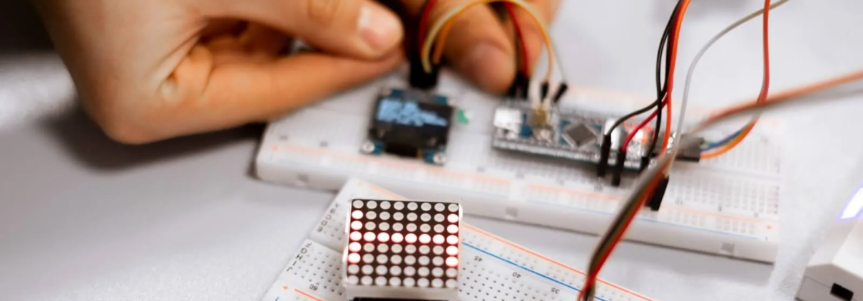 Hands assembling electronic components and wiring on a breadboard.