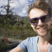 Man with sunglasses smiling outdoors in natural daylight.