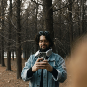 Smiling man in a forest taking a selfie with his phone.