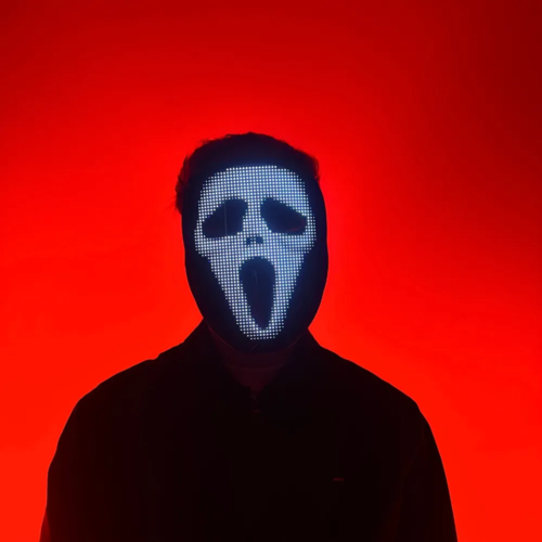 Person with an illuminated LED mask displaying a digital pattern, standing in front of a neon pink and blue background.